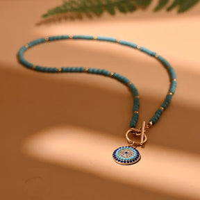 Beach-inspired evil eye necklace; Protective amulet jewelry; Handcrafted beach necklace; Coastal charm necklace; Natural stone beach accessory; Stylish summer jewelry; Boho beach necklace; Unique evil eye pendant; Symbol of protection and luck; Colorful beach-themed necklace; Perfect gift for beach lovers; Trendy ocean-inspired jewelry;